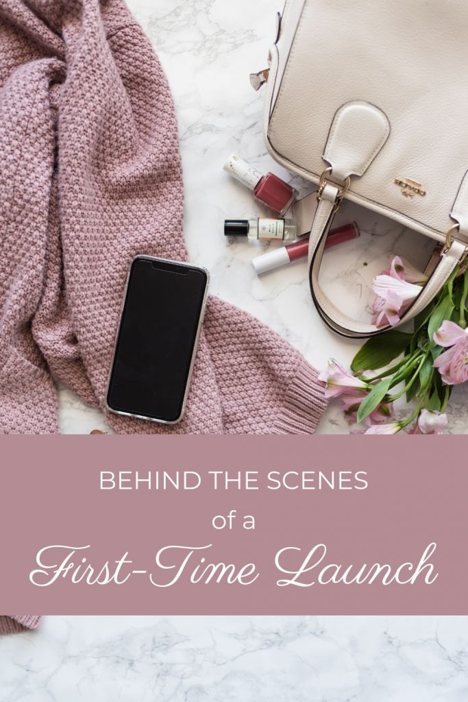 flat lay of sweater phone and purse with flowers and makeup text reads behind the scenes of a first time launch